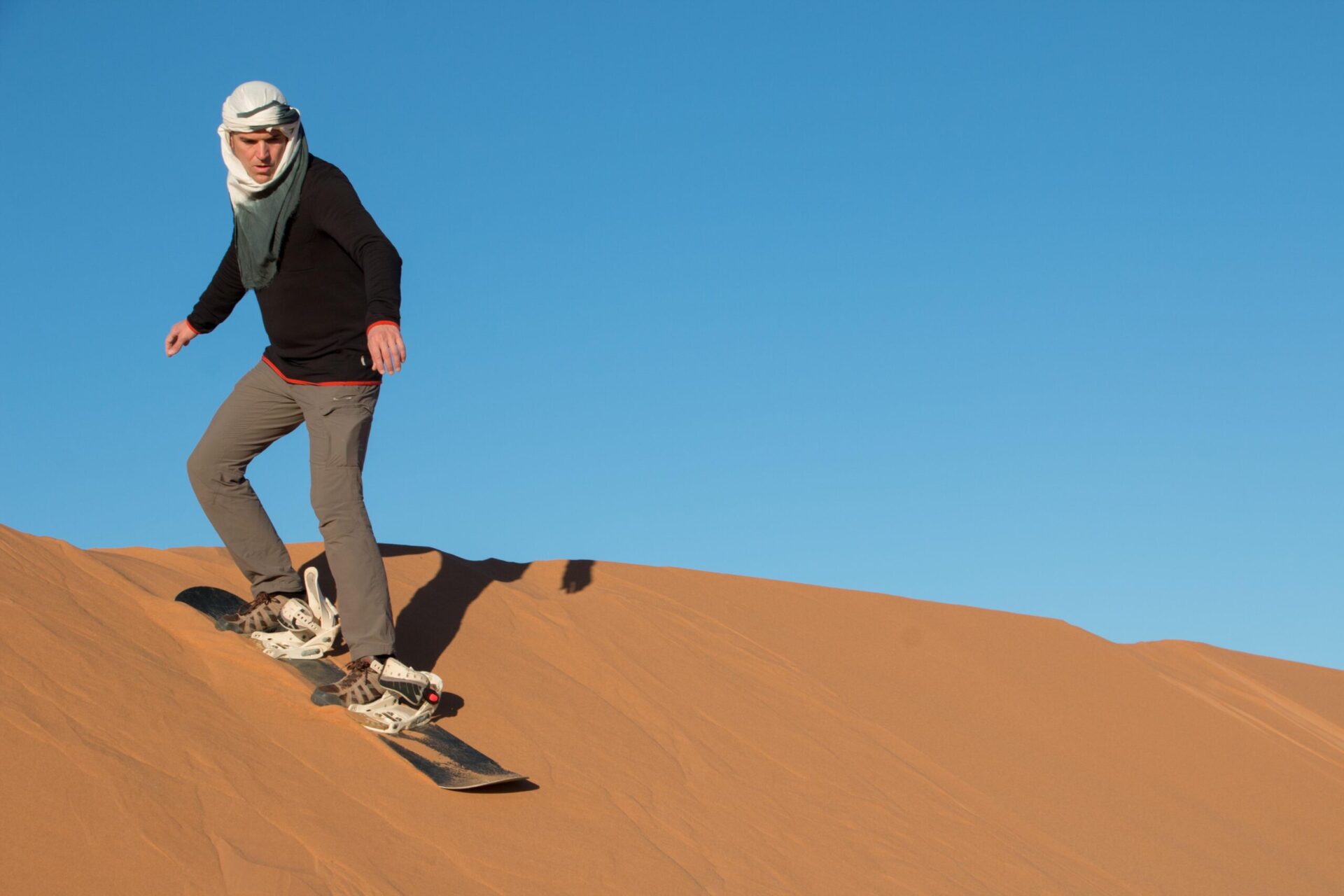 A man with a headscarf practicing sandboarding in the desert dunes of Erg Chebbi